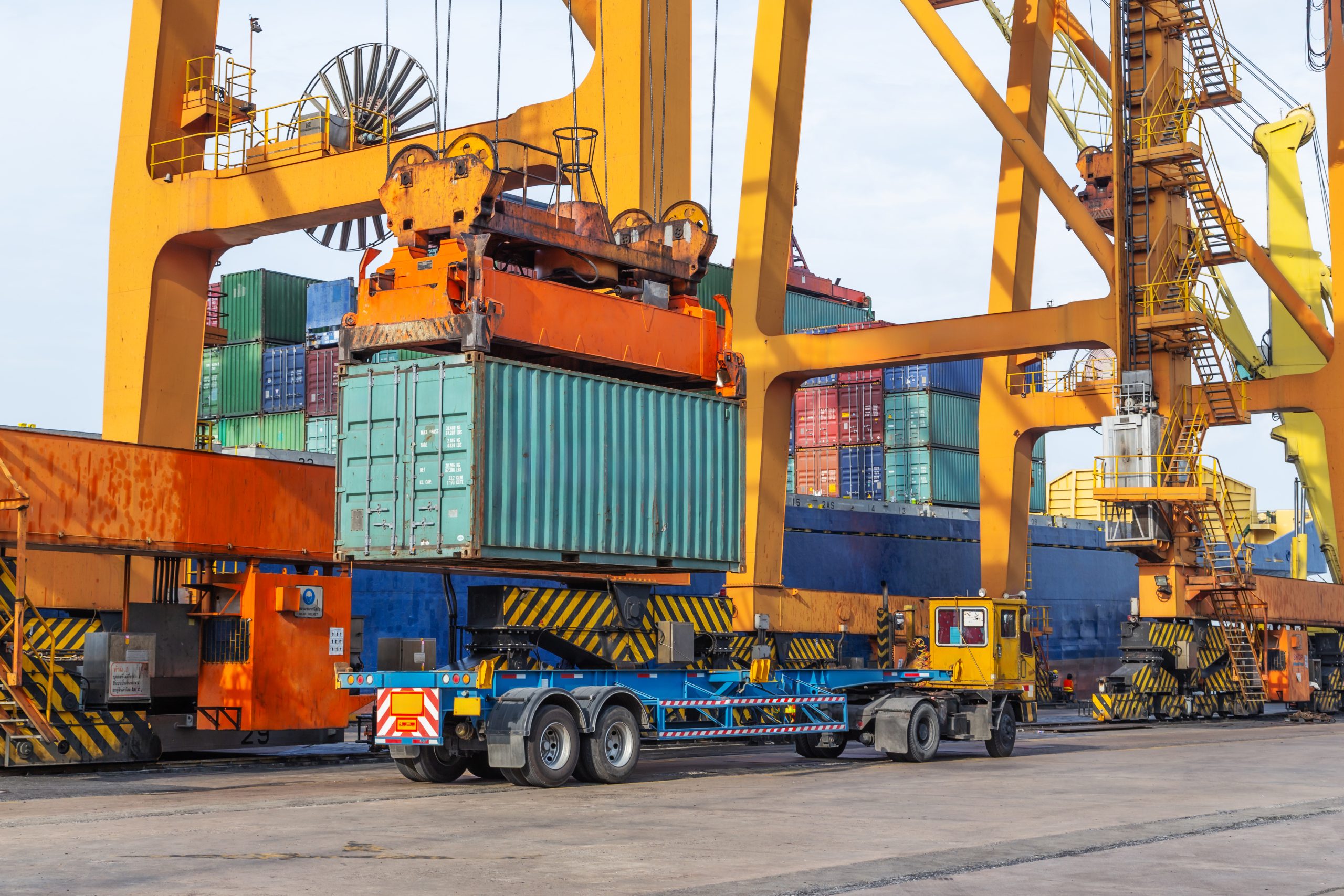 A port crane lifts a large shipping container onto a flatbed trailer, demonstrating the loading process essential for efficient import and export operations in global freight logistics.