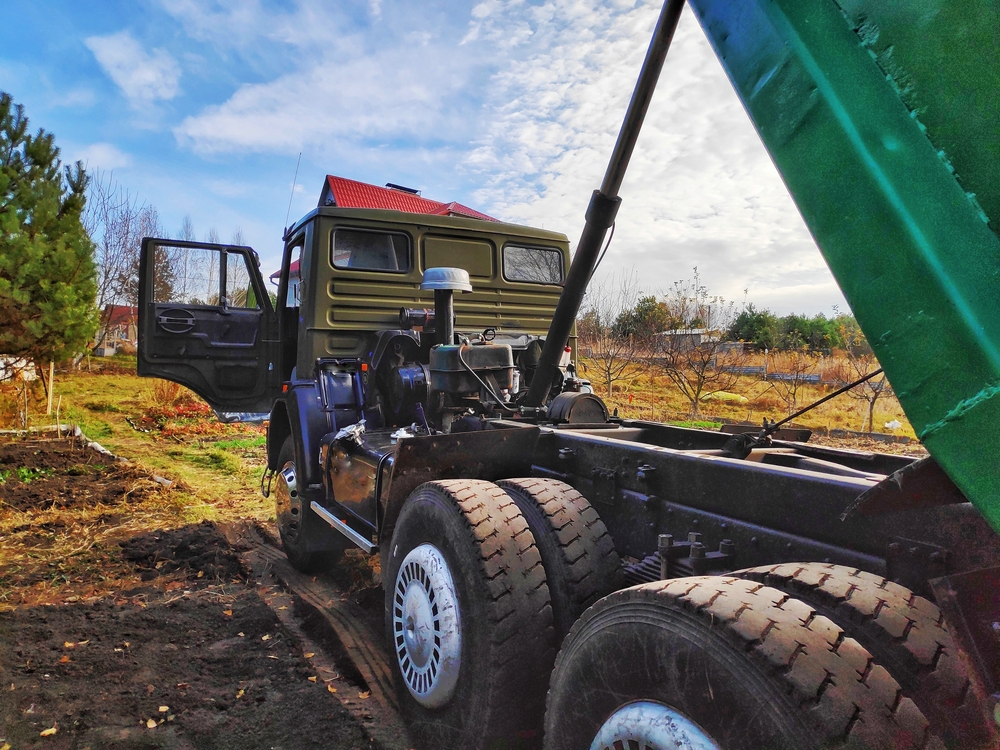 big green cargo dump truck car with body up on village