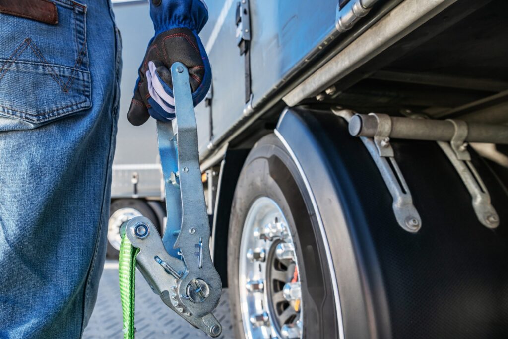Man Securing a Cargo Strap on a Truck at a Loading Dock During Daylight